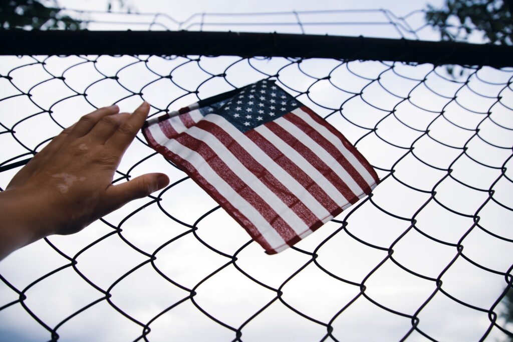 Hand holding america flag in front of a barbed fence. Illegal immigration concept.